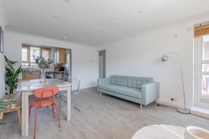 A modern living space with a dining area, a sofa, and a kitchen in the background.