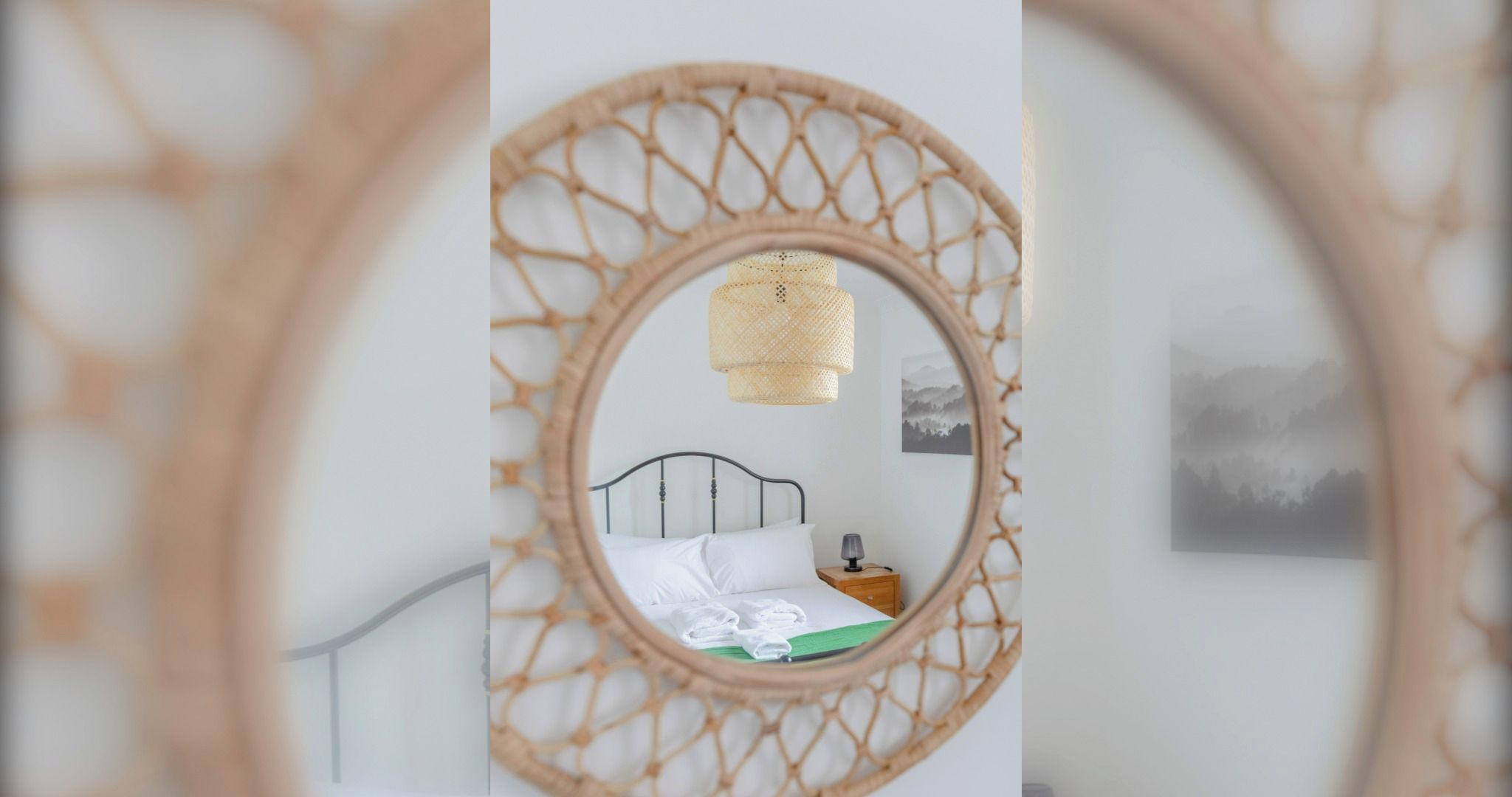 Une chambre avec un lit, une table de chevet, un miroir fixé au mur et un tableau encadré.