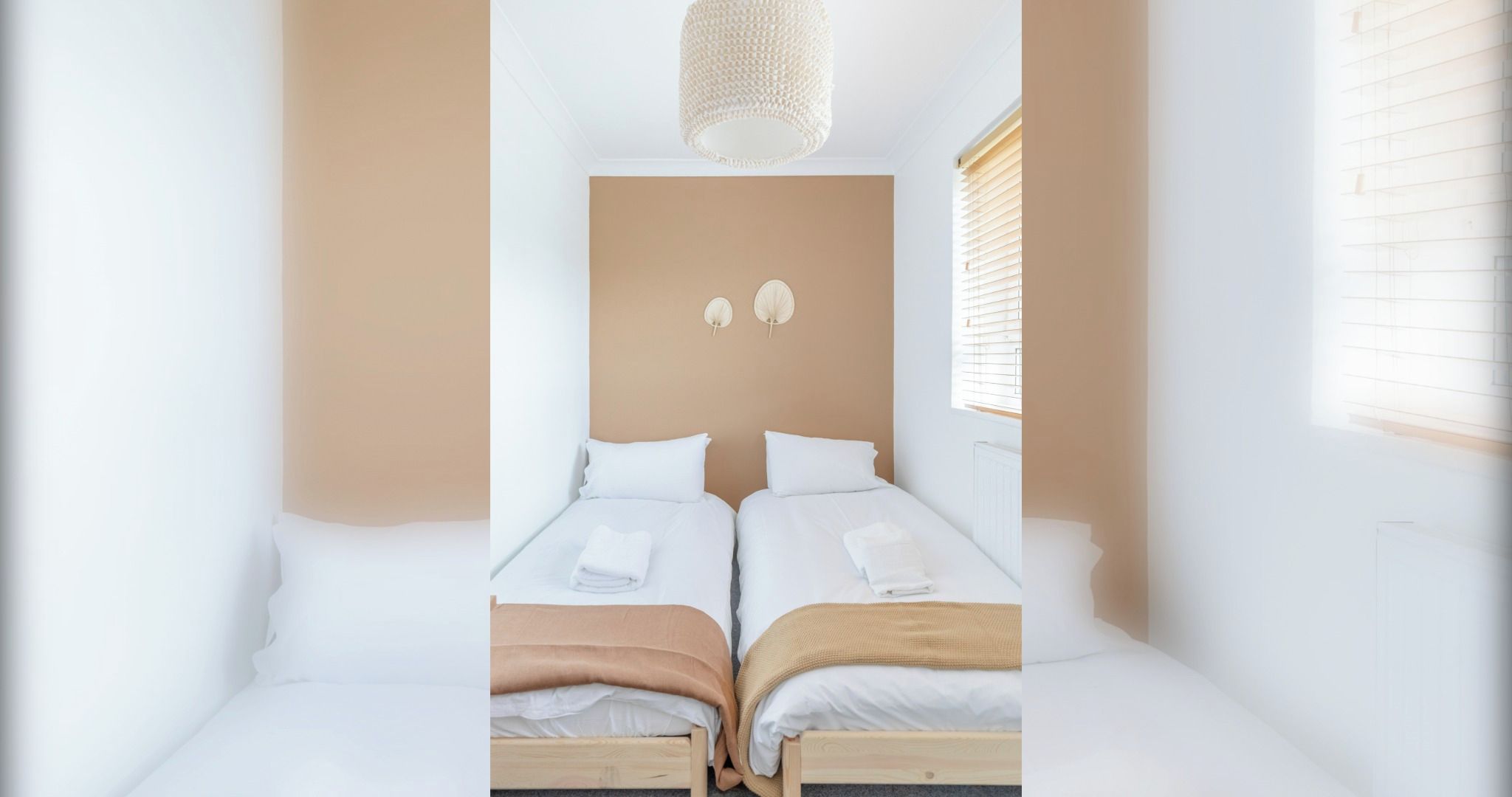 A bedroom with two beds, white bedding, a beige headboard, and a hanging light fixture.
