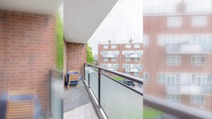 A balcony with a view of a brick building, a chair, and a small table.
