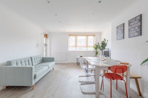 A modern living space with a sofa, dining table, chairs, and a large window.