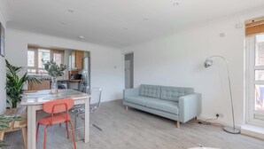 A modern living space with a dining area, sofa, and a kitchen in the background.