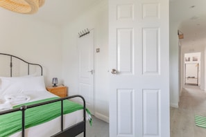 A hotel room with a bed, bedside table, lamp, and a door leading to another room.