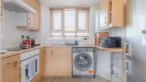 A compact kitchen with a washing machine, microwave, oven, and wooden cabinets.