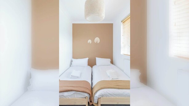 A room with two beds, a hanging light fixture, and a window with blinds.