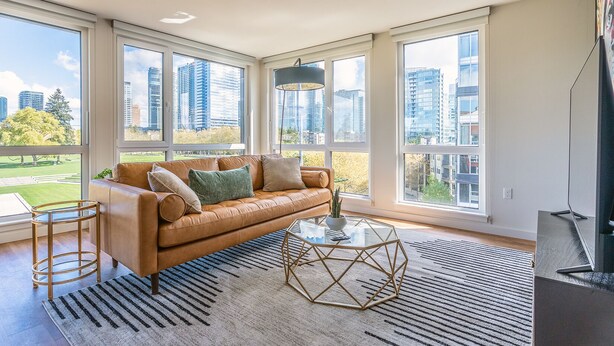 A modern living room with a leather sofa, a glass coffee table, and large windows offering city views. - Sophari Parkside: Bellevue Apartments (Bellevue)