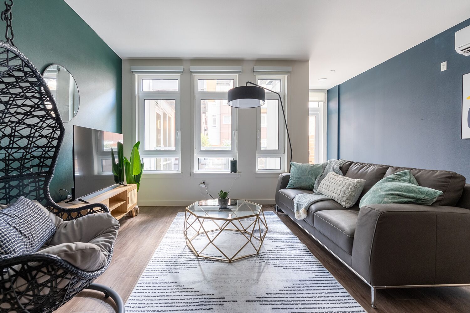 A modern living room with a sofa, a hanging chair, a coffee table, and a large window with multiple panes.