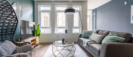 A modern living room with a sofa, a hanging chair, a coffee table, and a large window with multiple panes.