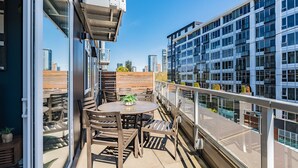 A balcony with a table and chairs, a glass door, and a view of a cityscape. - Sophari Parkside: Bellevue Apartments (Bellevue)