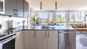 A modern kitchen with a central island, stainless steel appliances, and large windows offering a city view. - Sophari Parkside: Bellevue Apartments (Bellevue)