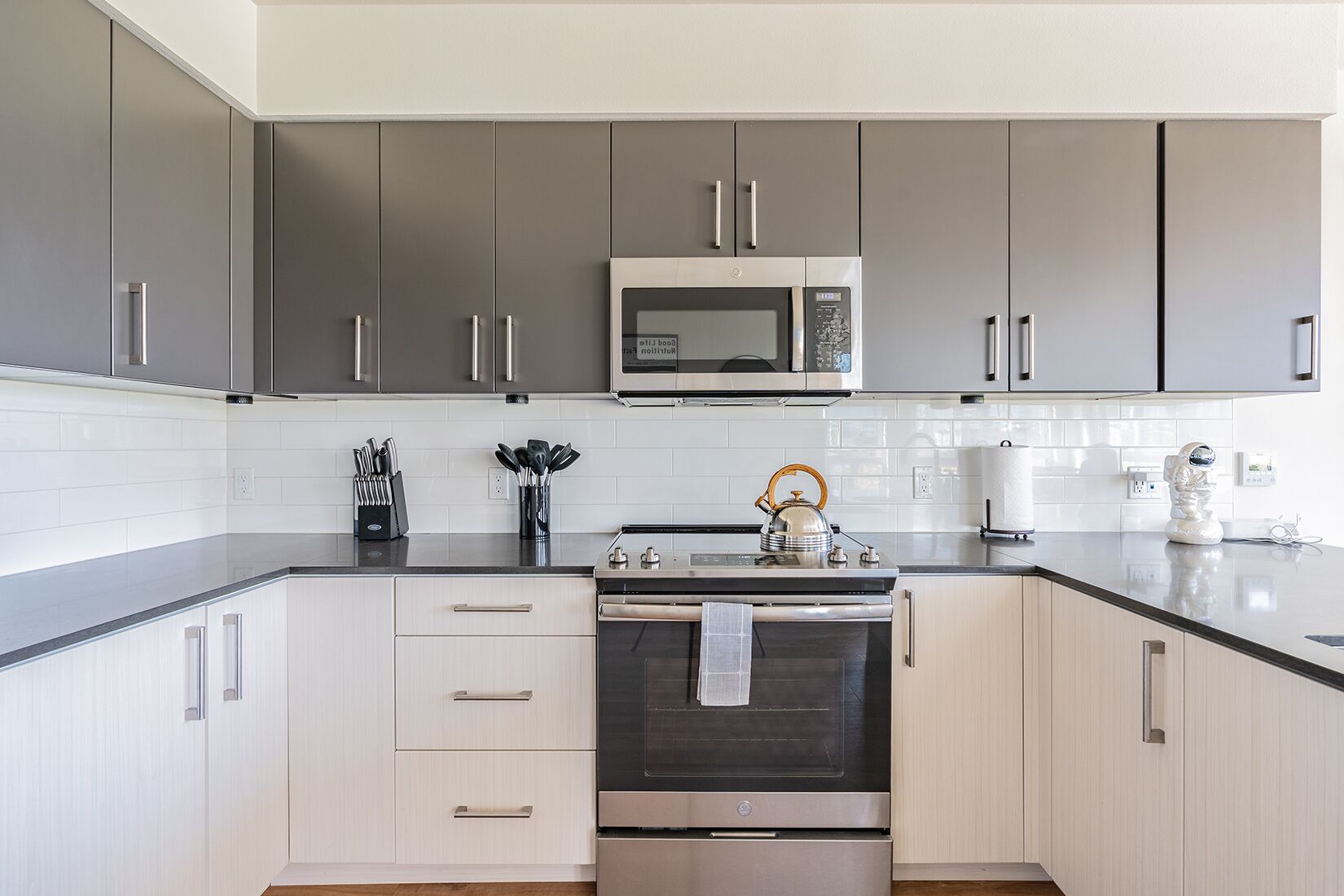 Una cocina moderna con armarios grises, un microondas de acero inoxidable, un hervidor y una cafetera.