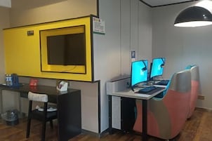 A room with a yellow accent wall, a desk with two monitors, a chair, and a hanging light fixture.