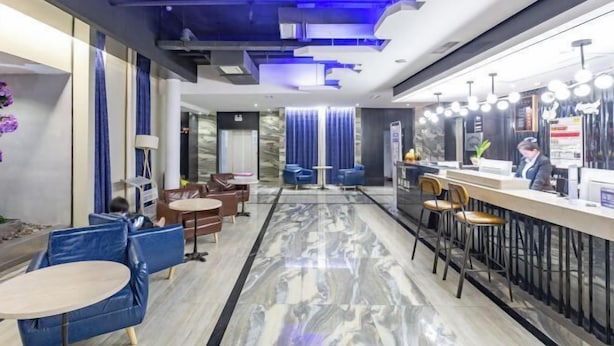 A modern hotel lobby with a marble floor, blue seating, and a reception area with a counter and chairs. - Zunyi Hengsheng Hotel (Yuqing)
