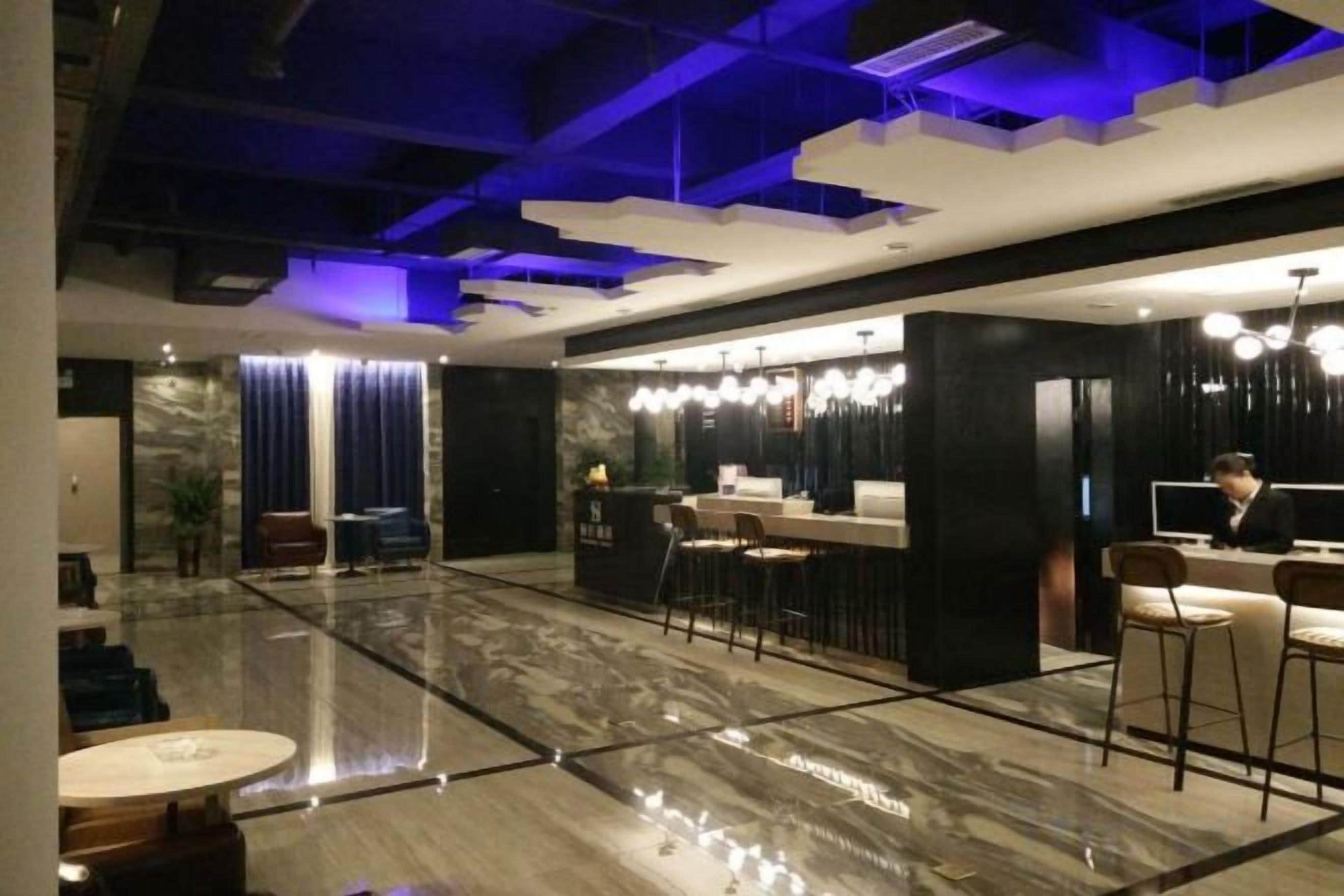 A modern hotel lobby with a marble floor, a reception desk, and bar seating.