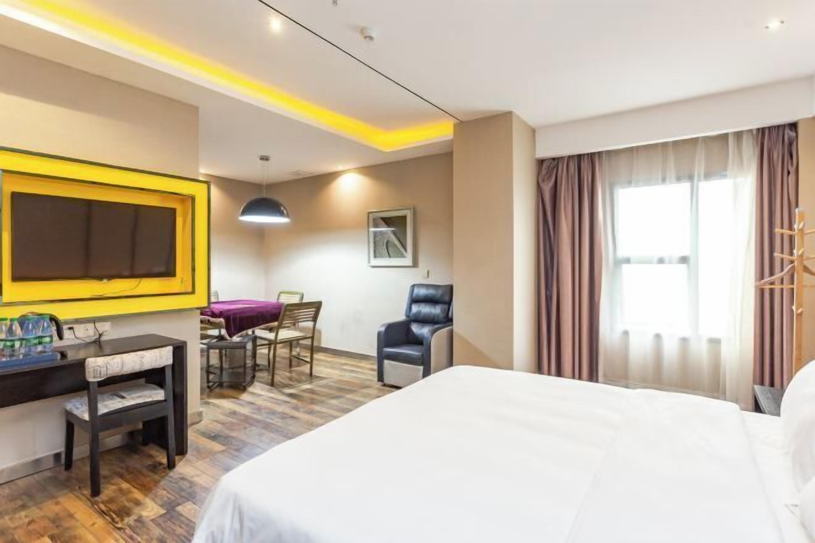A hotel room with a bed, a desk with a chair, a desk lamp, a chair, a TV, and a window with curtains.