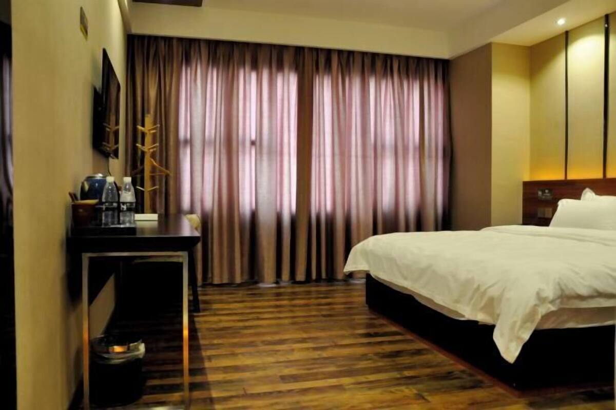 A hotel room with a large bed, a desk with a chair, a television, and a window with curtains.
