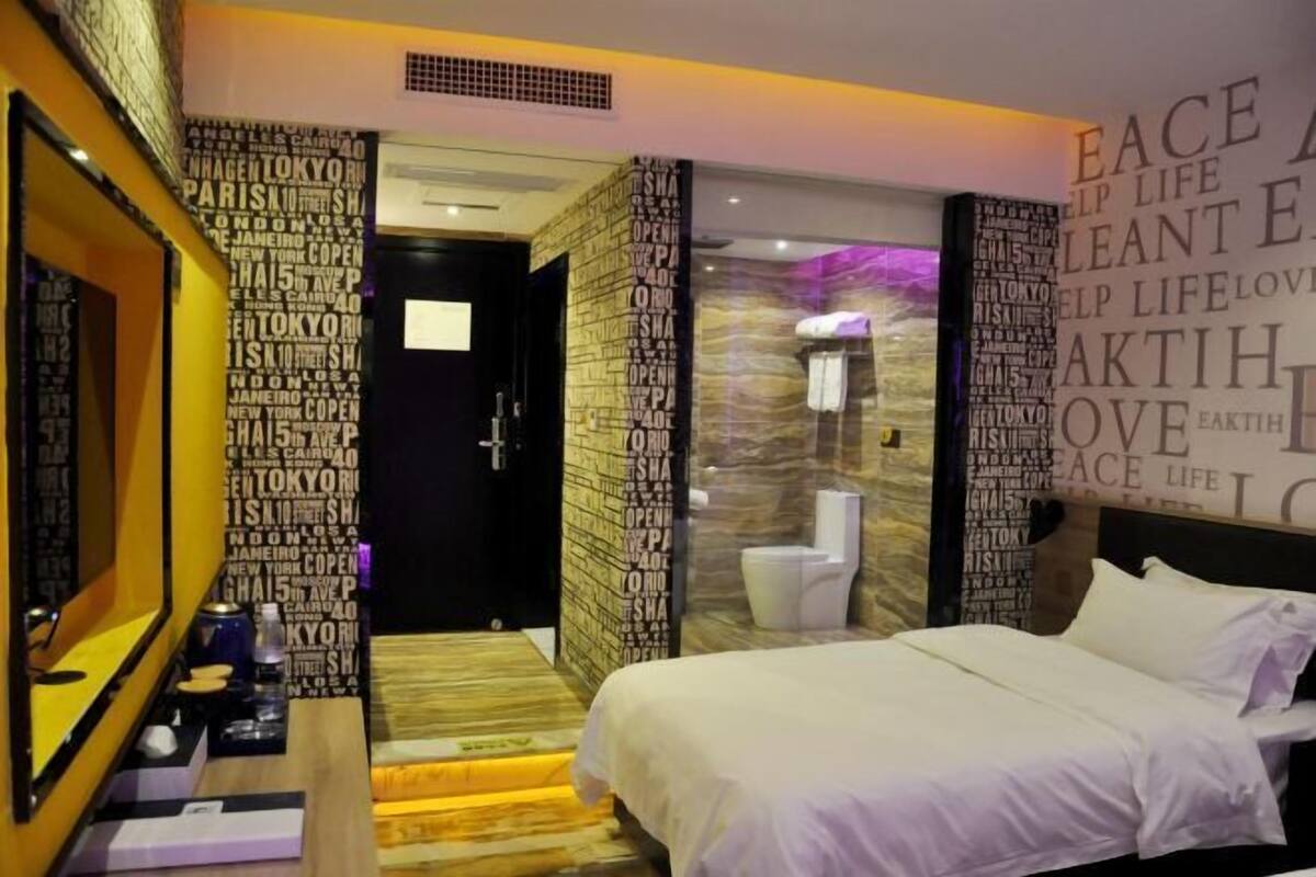 A hotel room with a bed, a desk with a computer, and a bathroom with a toilet and sink.