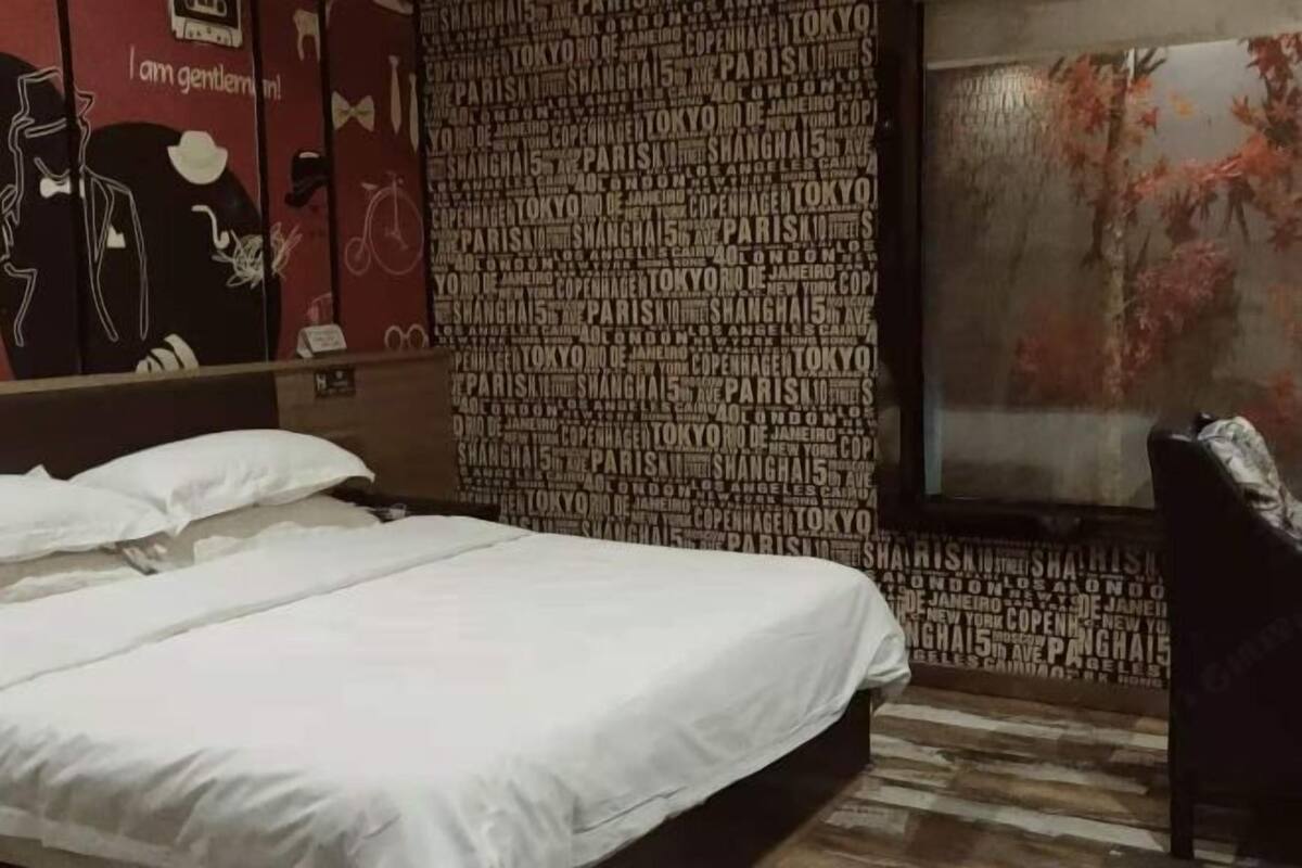 A hotel room with a bed, a chair, and a wall with city names.