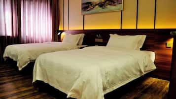 A hotel room with two beds, wooden flooring, a painting on the wall, and a curtain.