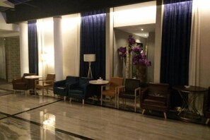 Un hall de hotel con una zona de estar, una lámpara y un florero con flores.