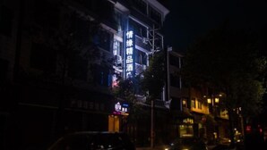 Un edificio con señalización iluminada en la noche, que destaca un letrero vertical con texto.