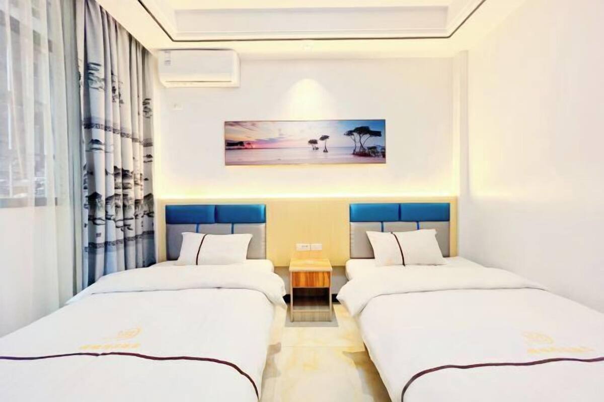 A hotel room with two beds, a nightstand, a painting on the wall, and a window with curtains.
