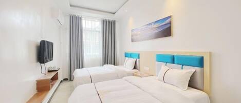 A hotel room with two beds, a TV, a painting, and a window with curtains.