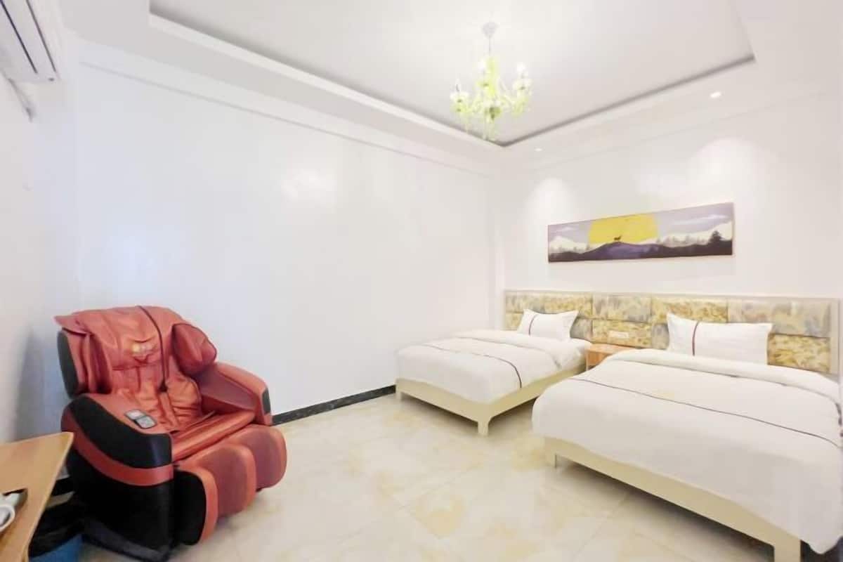 A hotel room with two beds, a massage chair, a painting on the wall, and a chandelier.