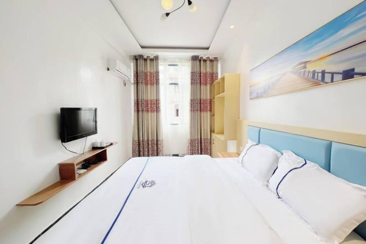 A hotel room with a bed, a TV, a shelf, and a painting on the wall.