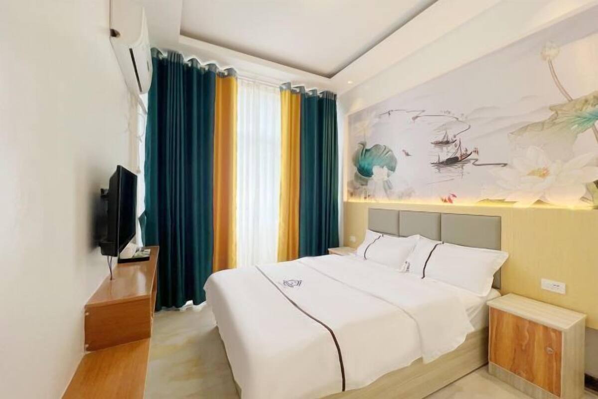 A hotel room with a bed, a TV, a nightstand, and a wall with a painting.