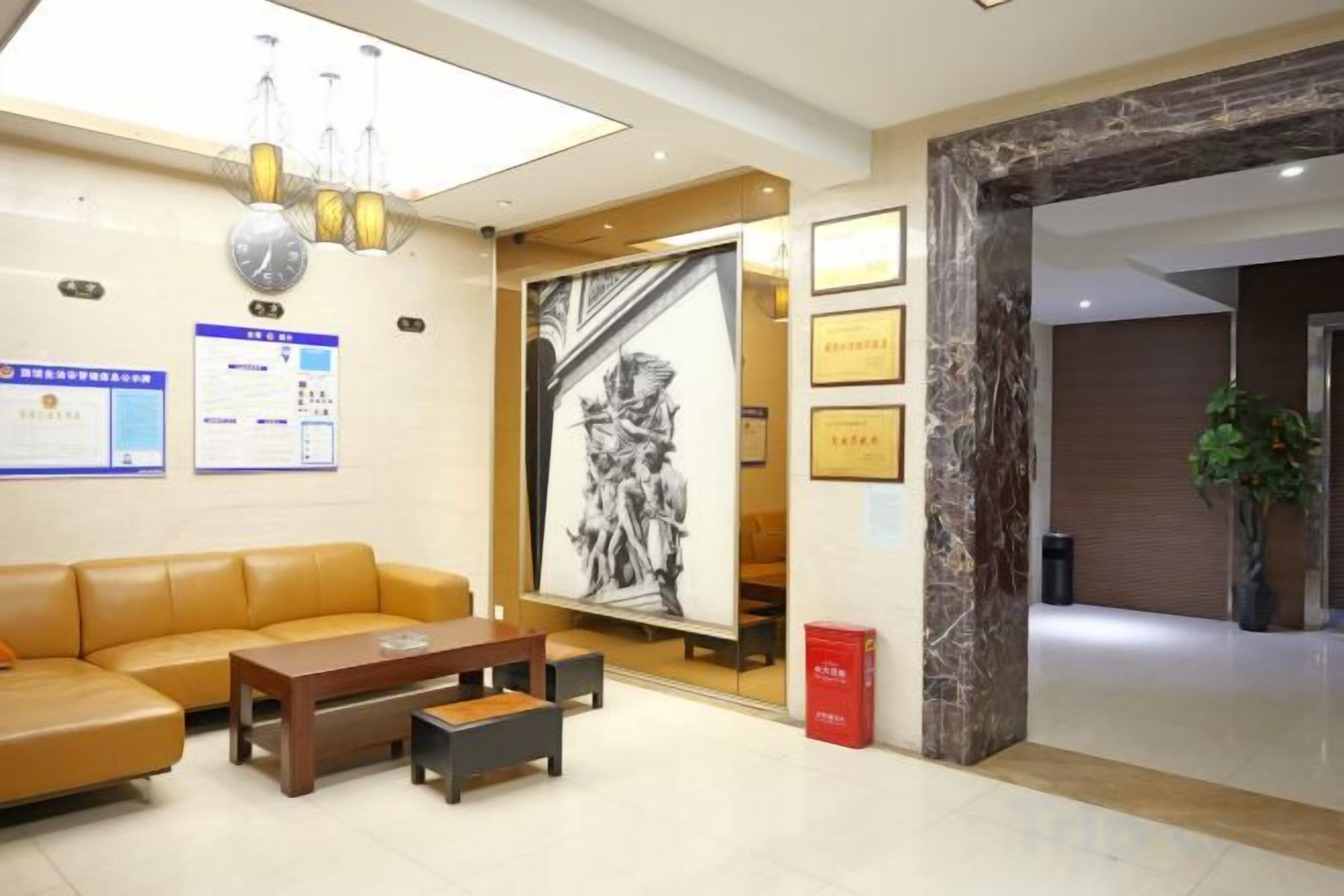 A hotel lobby with a sofa, a coffee table, a reception desk, framed certificates, and a large black-and-white artwork.