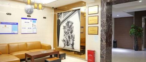 A hotel lobby with a sofa, a coffee table, a reception desk, framed certificates, and a large black-and-white artwork.