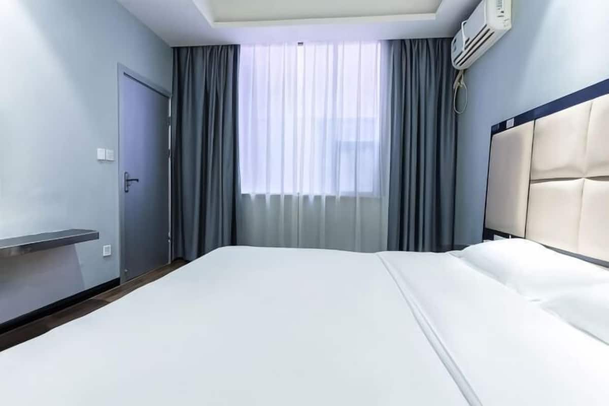 Une chambre d’hôtel avec un lit, une porte, une fenêtre avec des rideaux et un climatiseur fixé au mur.