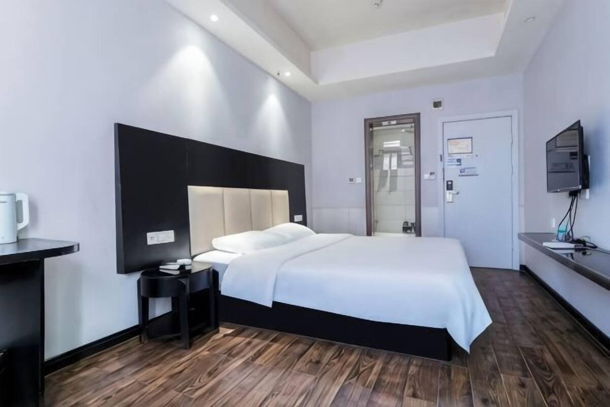 Une chambre d’hôtel moderne équipée d’un lit, d’une table de chevet, d’une télévision et d’une porte donnant accès à une salle de bain.