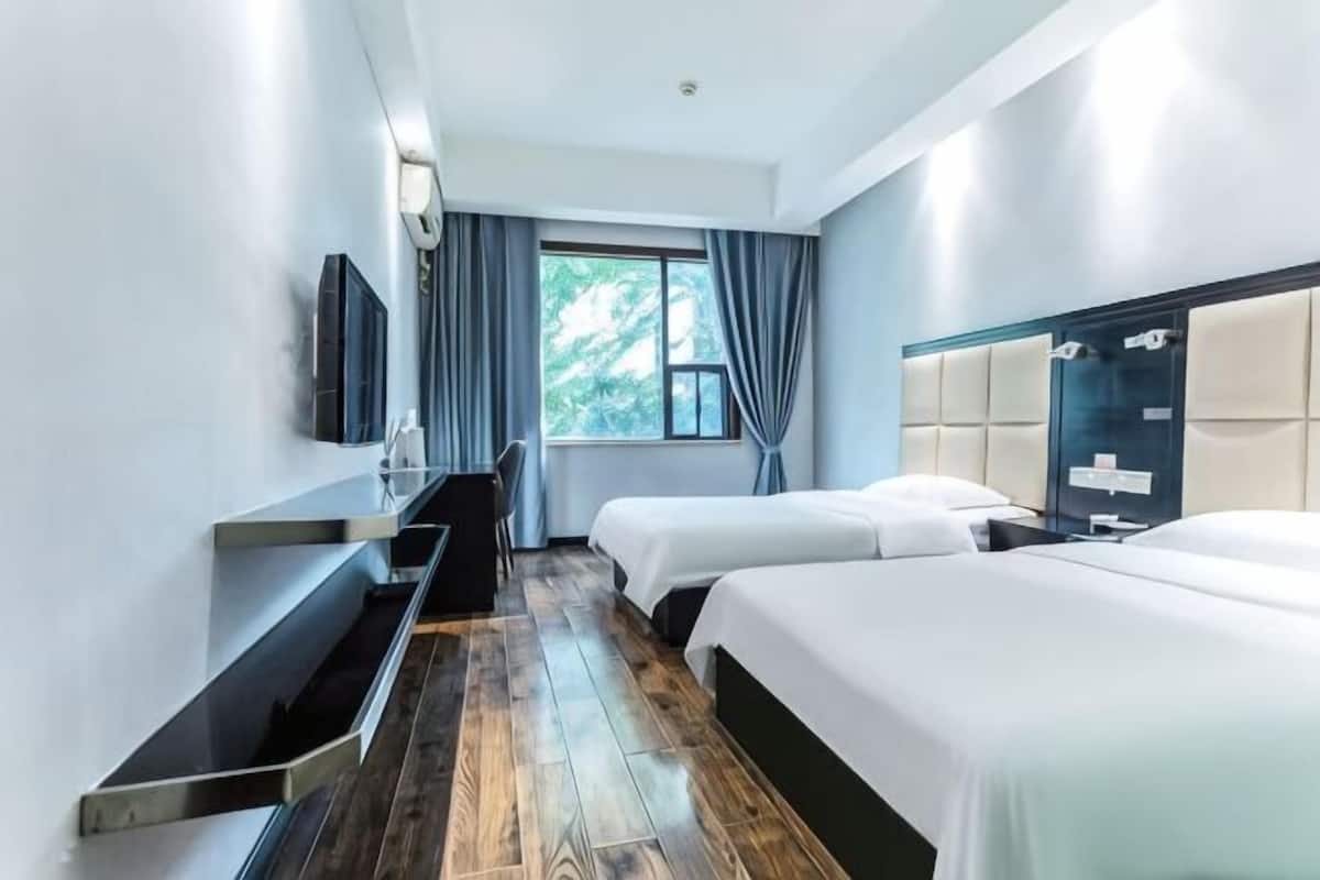 Une chambre d’hôtel avec deux lits, un téléviseur fixé au mur, un bureau et une fenêtre avec des rideaux.