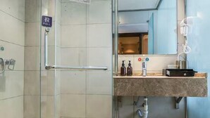 Een moderne badkamer met een glazen douchecabine, een handgreep, een wastafelmeubel met spiegel en een haardroger aan de muur.
