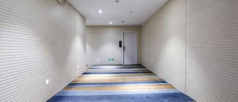 A corridor with a patterned carpet, a door at the end, and walls with a textured finish.