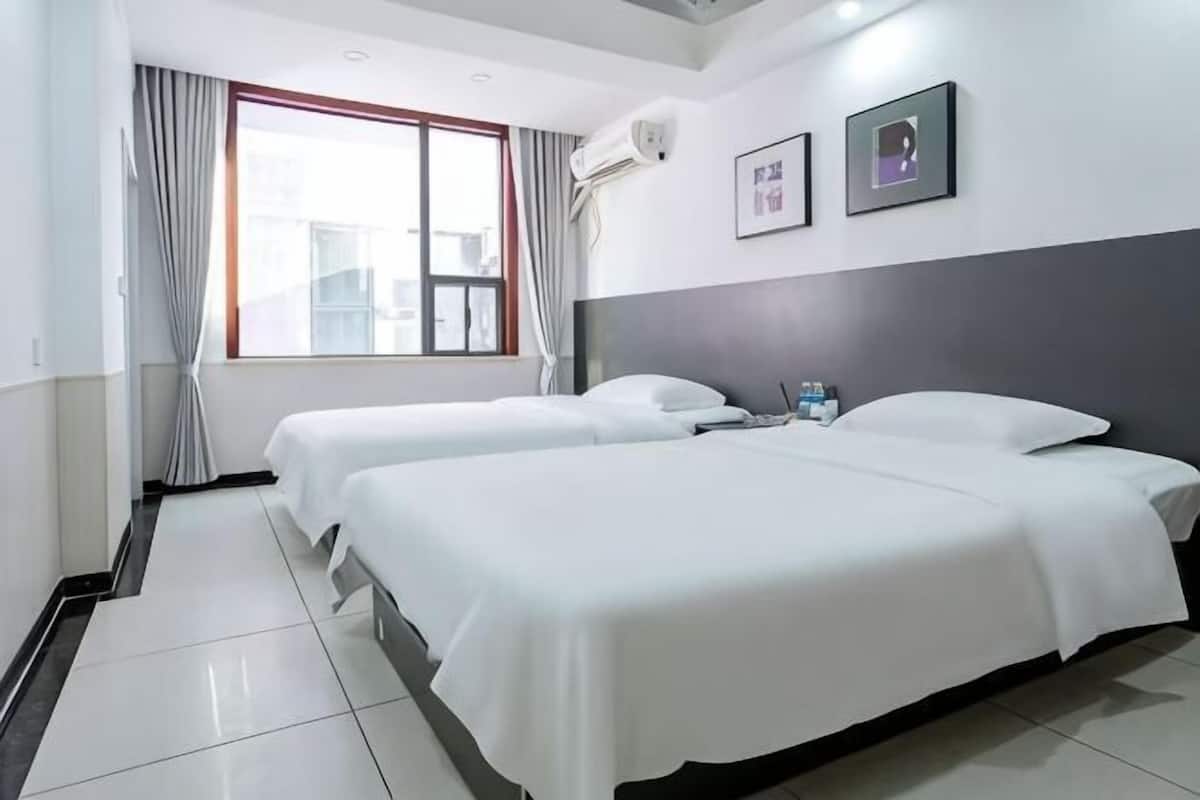 Une chambre d’hôtel avec deux lits, une fenêtre avec des rideaux, un appareil de climatisation et des tableaux encadrés au mur.