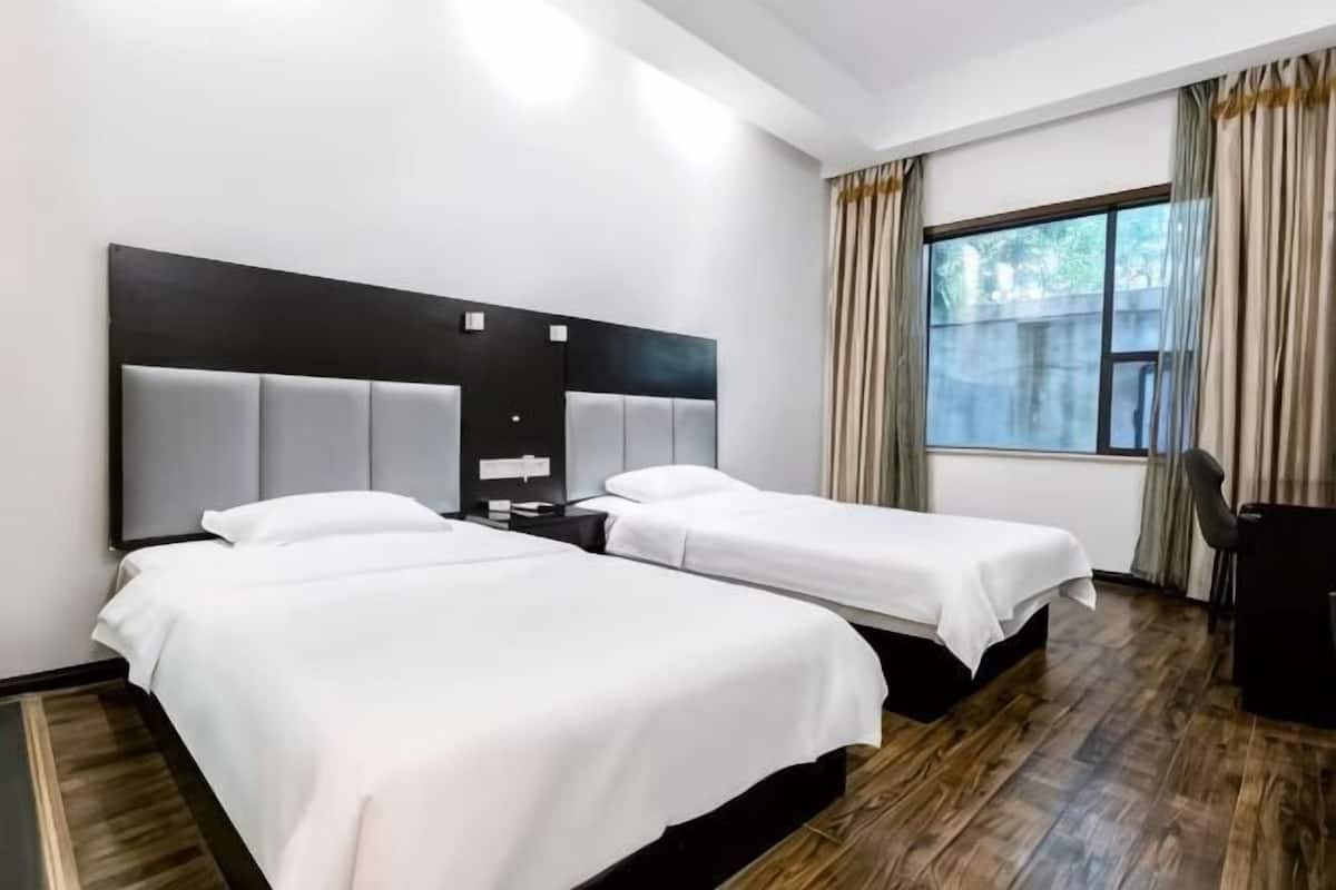 Une chambre d’hôtel avec deux lits, un bureau, une chaise et une fenêtre avec des rideaux.