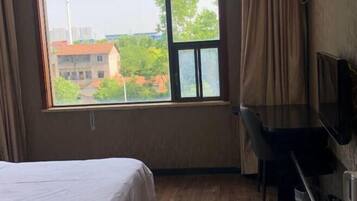 Een hotelkamer met een bed, een bureau en een groot raam met uitzicht op gebouwen en bomen.