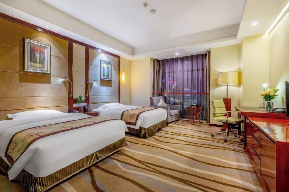 A hotel room with two beds, a desk, a chair, and a large window with curtains.
