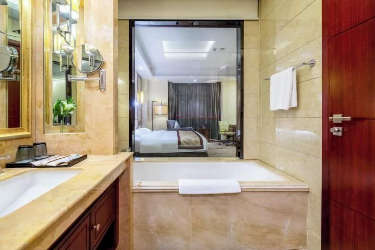 A hotel bathroom with a large mirror, a sink, a bathtub, and a door leading to a bedroom.