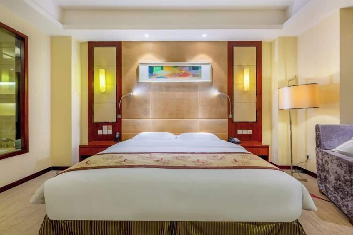A hotel room with a large bed, a headboard with a painting, a bedside table, a lamp, and a chair.