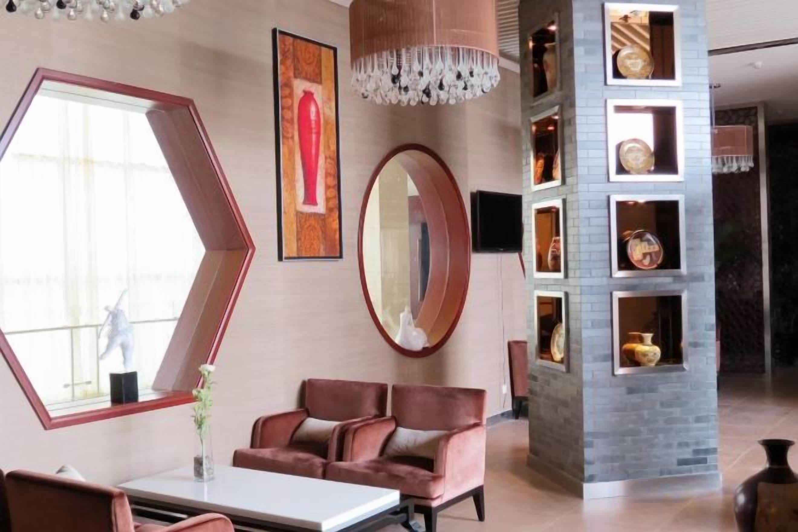 A modern interior with a hexagonal mirror, a round mirror, and a wall with shelves displaying decorative items.
