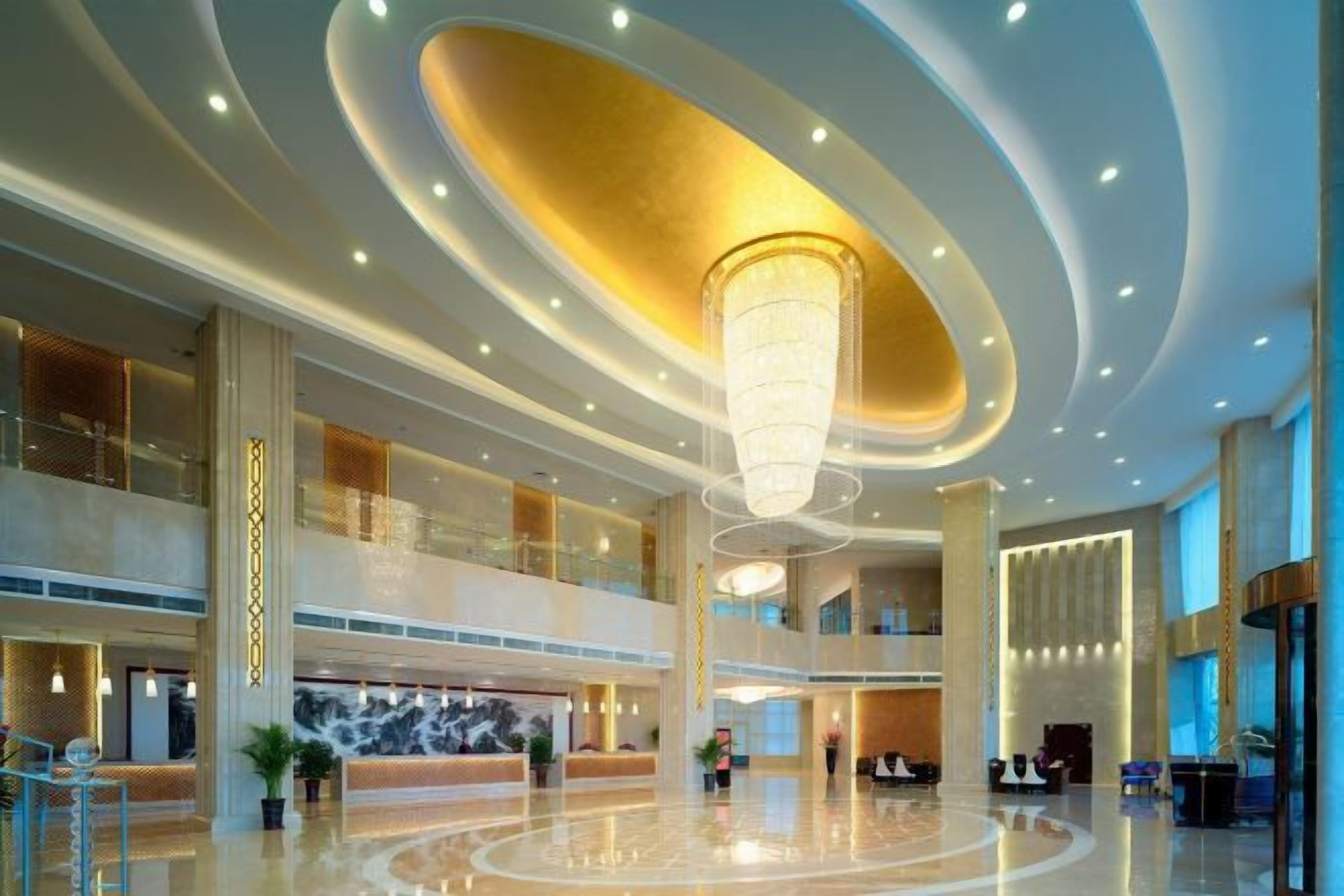 A spacious lobby with a central chandelier, a reception desk, and multiple floors.