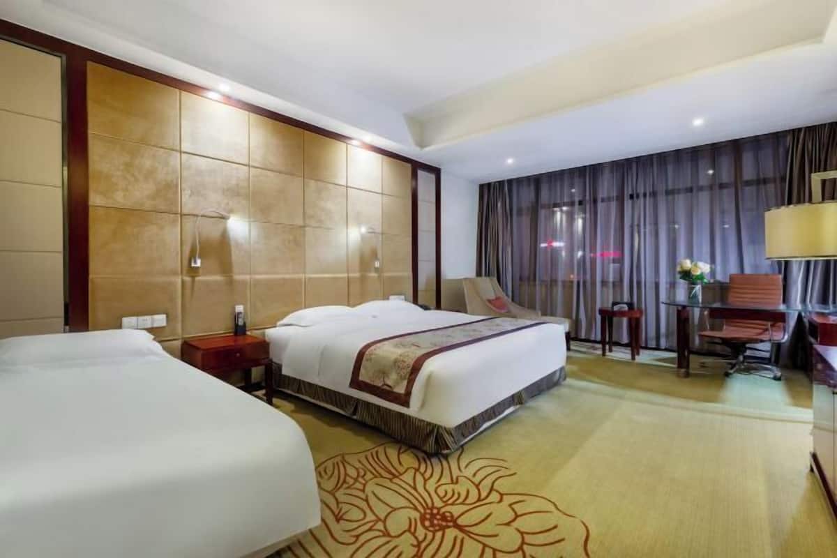 A hotel room with two beds, a desk, a chair, a lamp, and a large window with curtains.