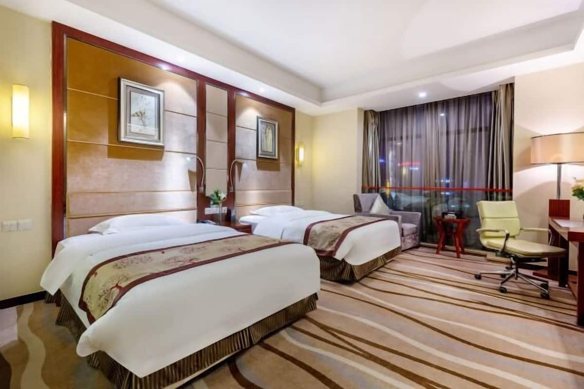 A hotel room with two beds, a desk, a chair, and a large window with curtains.
