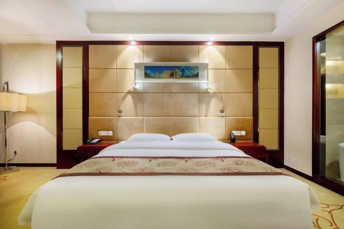 A hotel room with a large bed, a nightstand, a lamp, and a painting on the wall.