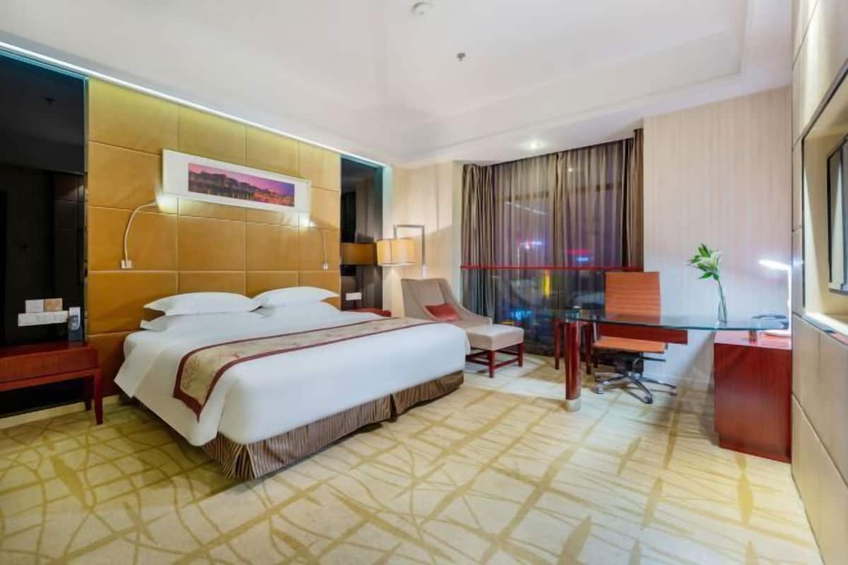 A hotel room with a large bed, a desk, a chair, a lamp, and a window with curtains.