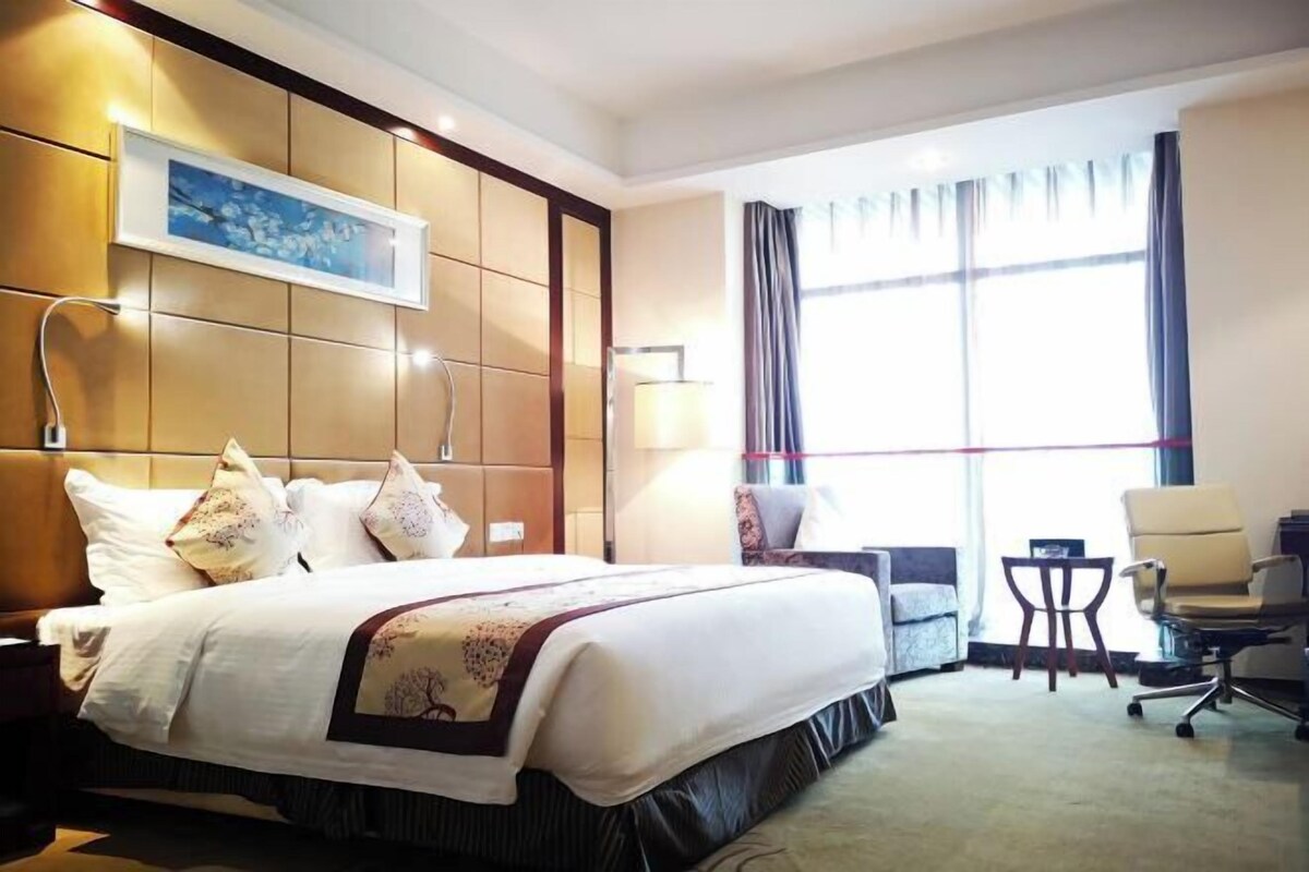 Una habitación de hotel con una cama grande, un escritorio, una silla y un ventanal con cortinas.